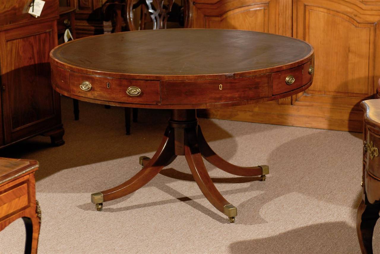 A 19th Century Mahogany Drum Table with Gold Embossed Brown Leather Top,  Four Drawers, Pedestal Base terminating in 4 Splay Legs with Brass Feet and Castors.  Dating from the Early 19th century and English in Origin.