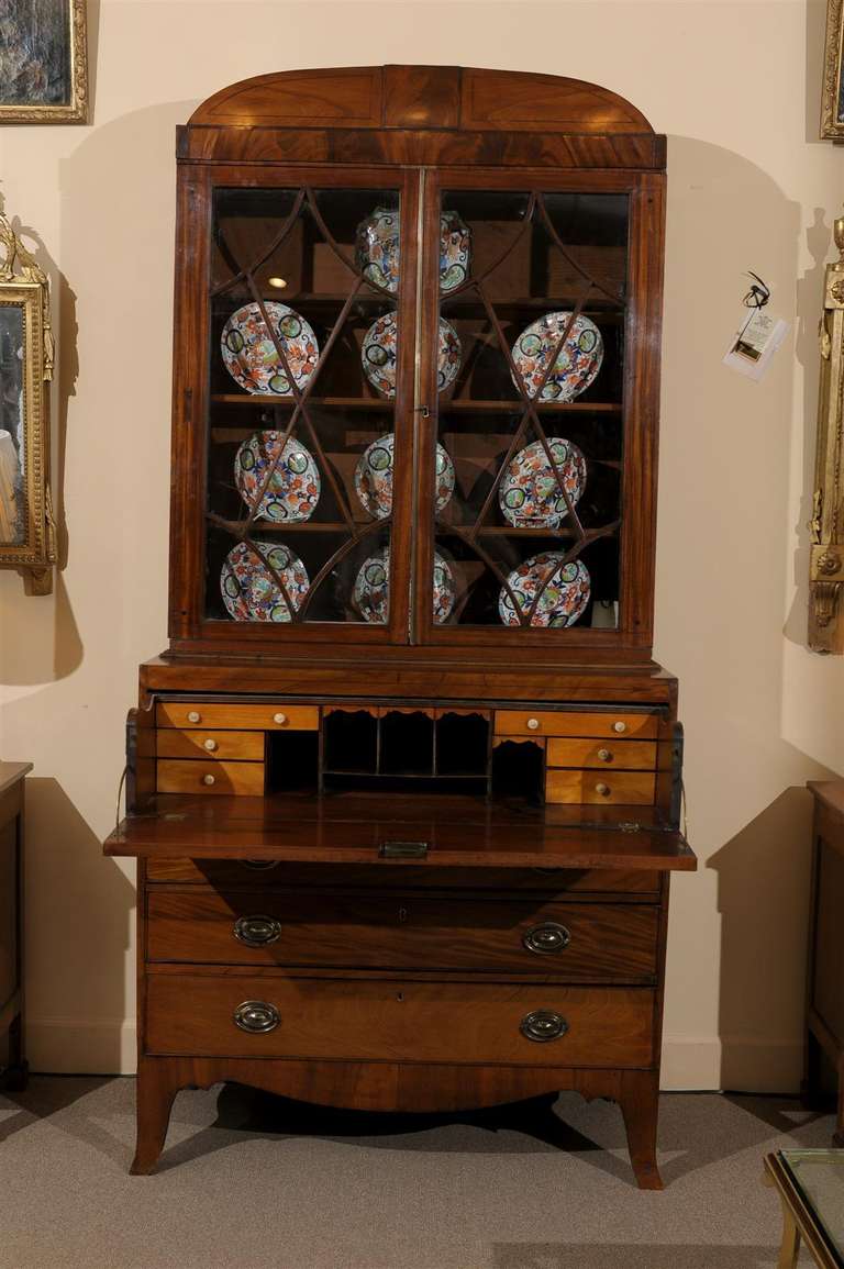 An Early 19th century Mahogany secretary with arched cornice, string inlay, sash work on glass paned cabinet and secretary drawer below enclosing fitted interior with pigeon holes, satin wood drawers and writing surface. Below are 3 sliding drawers