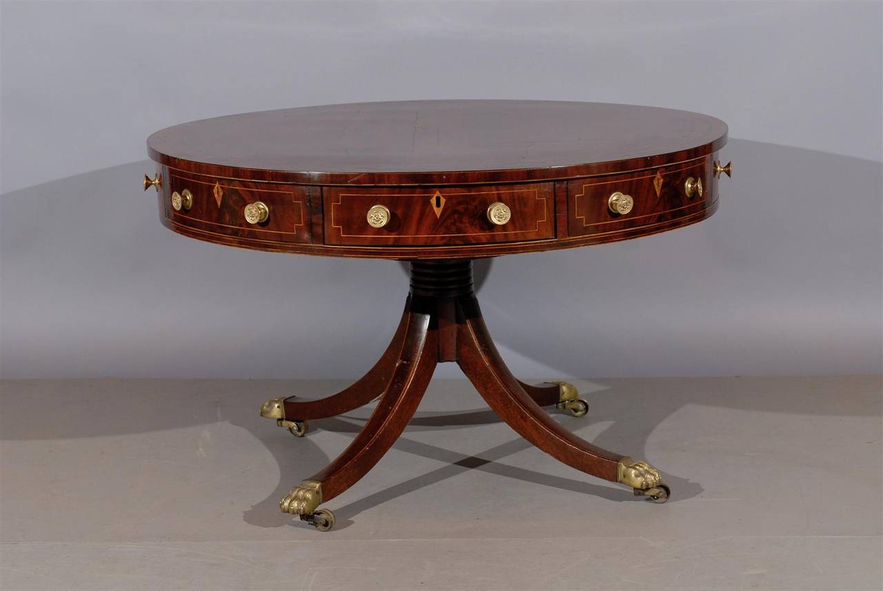 An English mahogany rent table with string boxwood inlay, four sliding drawers, pedestal base with brass paw feet and castors. 


