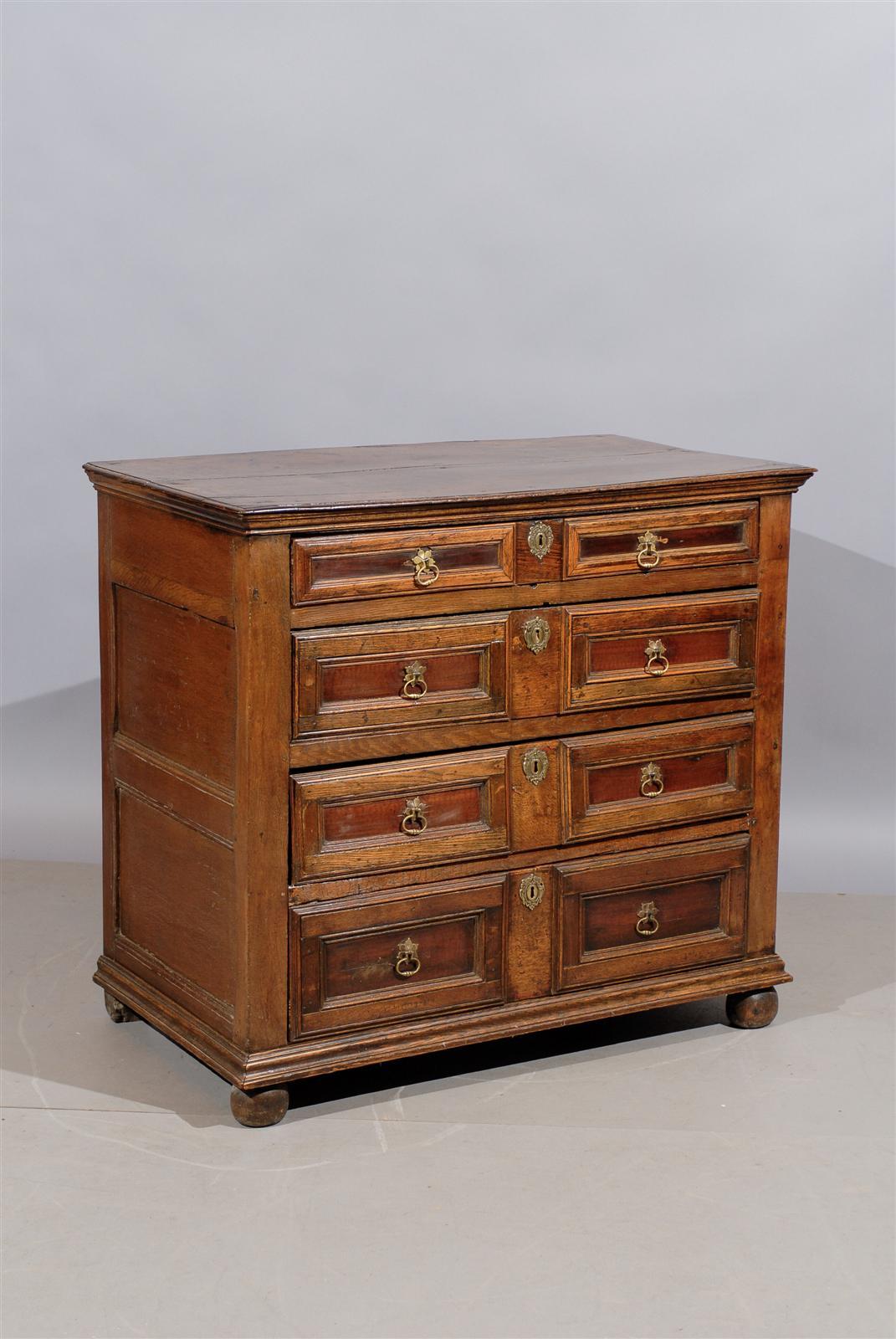 An 18th century English Jacobean style oak chest with four graduated drawers, paneled ends and bun feet.