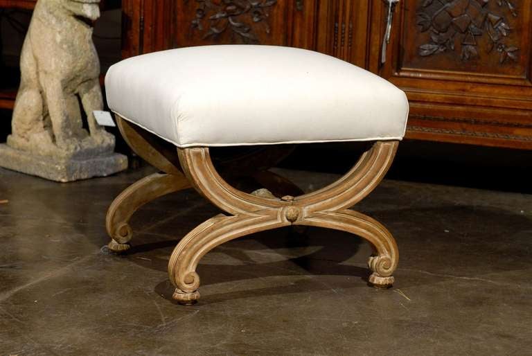 This French vintage upholstered stool features an exquisite X-frame body made of two reversed demilune supports. The feet are nicely scrolled and slightly raised. Each leg support is connected to each other with a carved cross stretcher with foliage