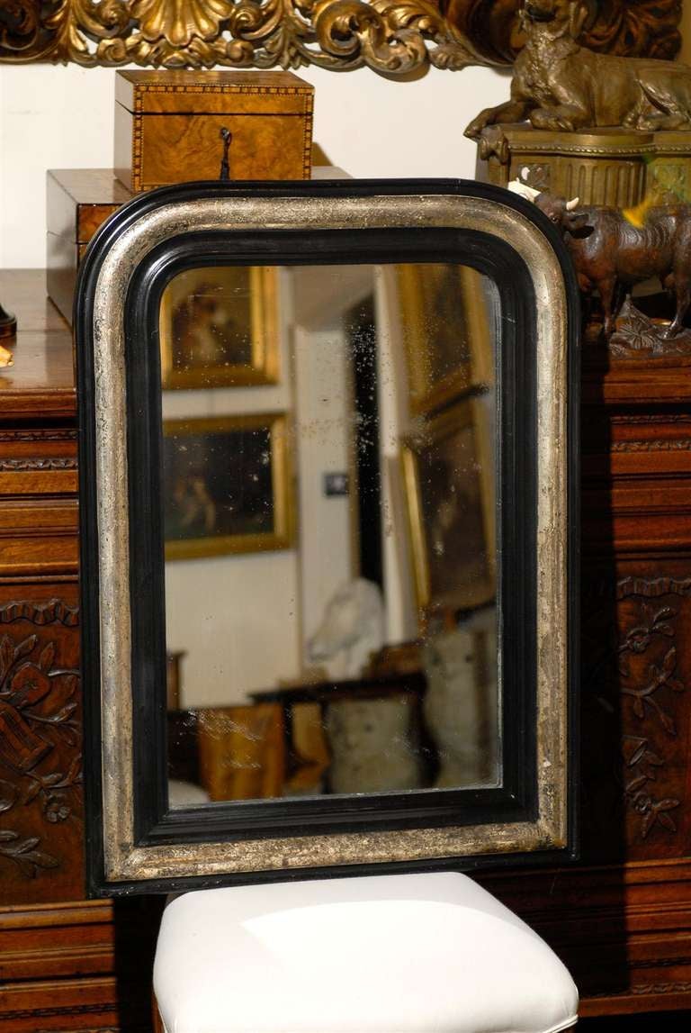 A medium size French ebonized wood and silver gilt Louis-Philippe mirror from the early 20th century. This French mirror features the typical silhouette of Louis-Philippe mirrors: a vertical rectangular shape, softened in the upper section by