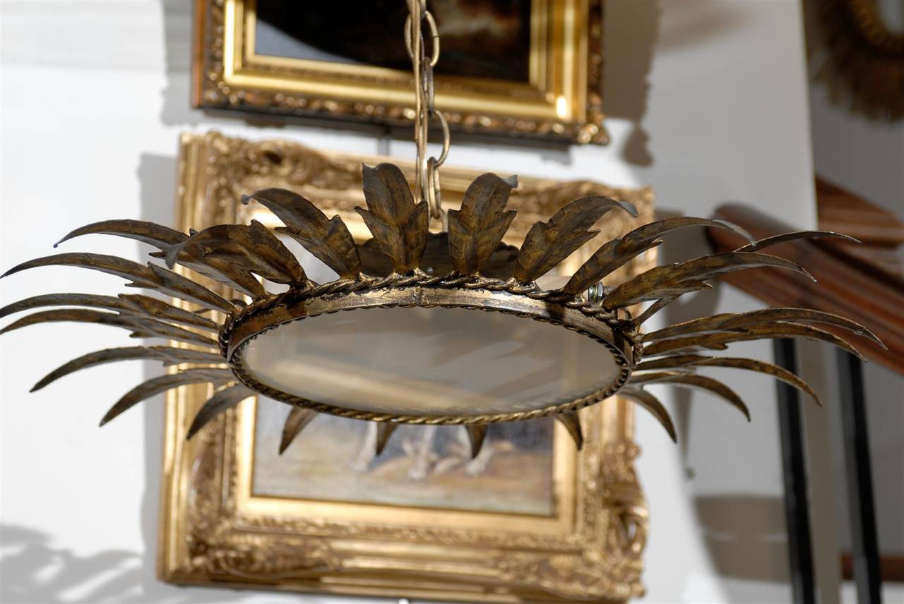 This Spanish gilt metal two-light fixture from the mid-20th century features a round shape, embellished by metal leaves. The bottom part is adorned with frosted glass, secured with a metal ring decorated on the inside and on the outside by