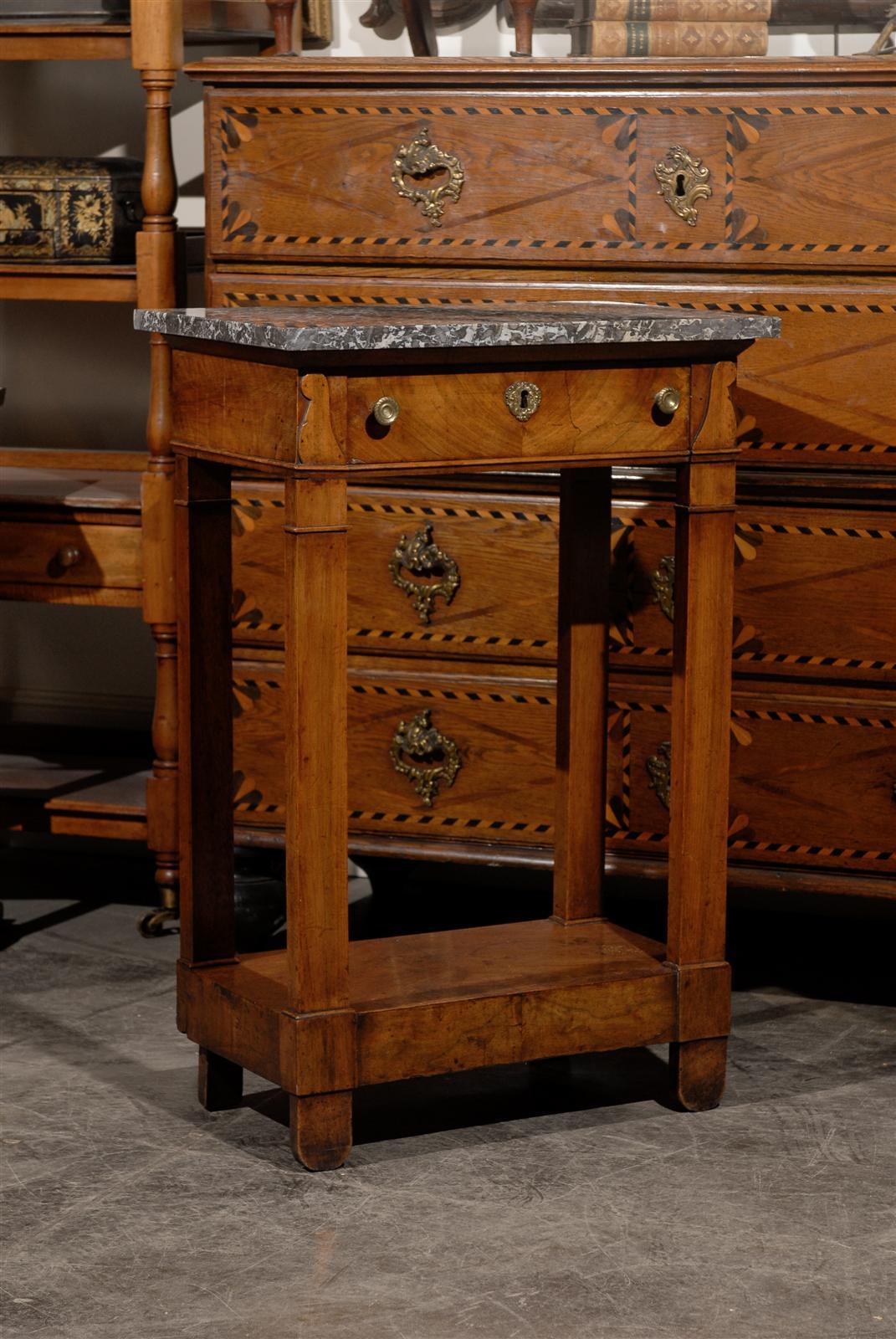 This French petite Empire style walnut veneered console table from the first half of the 19th century features a rectangular grey veined marble top over a single dovetailed drawer. The drawer features a butterfly veneer, brass hardware and discreet