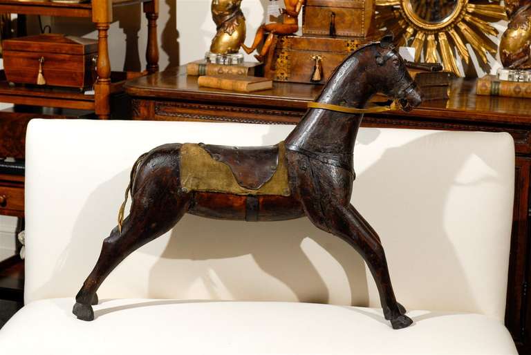 This mid-19th Victorian antique painted carved and assembled wooden child's horse has its back covered with a leather saddle and a saddle blanket made of cloth, embroidered with the letters W and K on each side. The tactile ears, mane and tail as