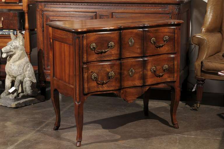 This mid-19th century French Louis XV style wooden two-drawer serpentine commode features a rectangular molded top with an arbalette-shaped cornice and frieze continued on the paneled sides. The elegant serpentine front is fitted with two drawers