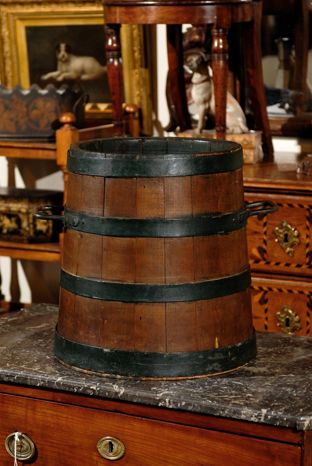 This large size English bucket, circa 1880 features a circular shape, flaring towards the bottom with four iron bands wrapped around the wooden slats. Two iron handles on each side make for easy moving. This English bucket could be used as storage,