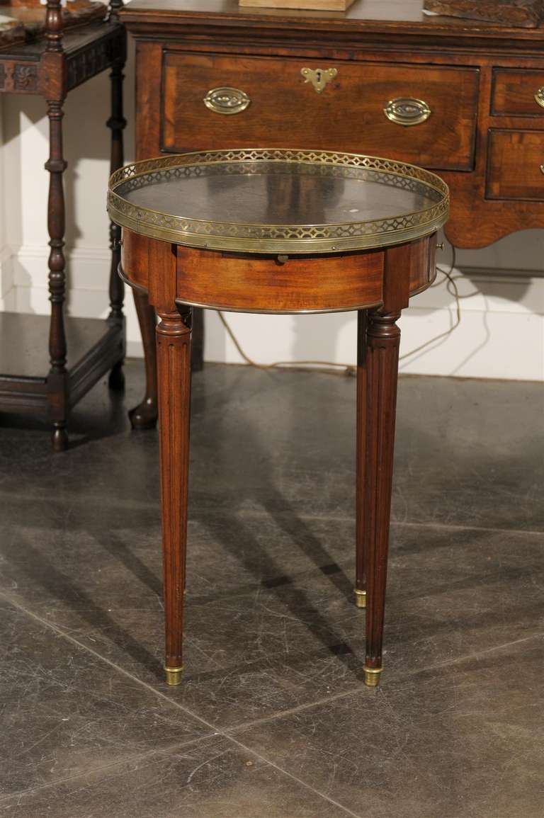 A French round bouillotte game table with brass gallery, marble top, two drawers and two leather pull outs from the early 19th century. This delicate bouillotte French table circa 1820 features a rounded marble top with brass gallery on a simple