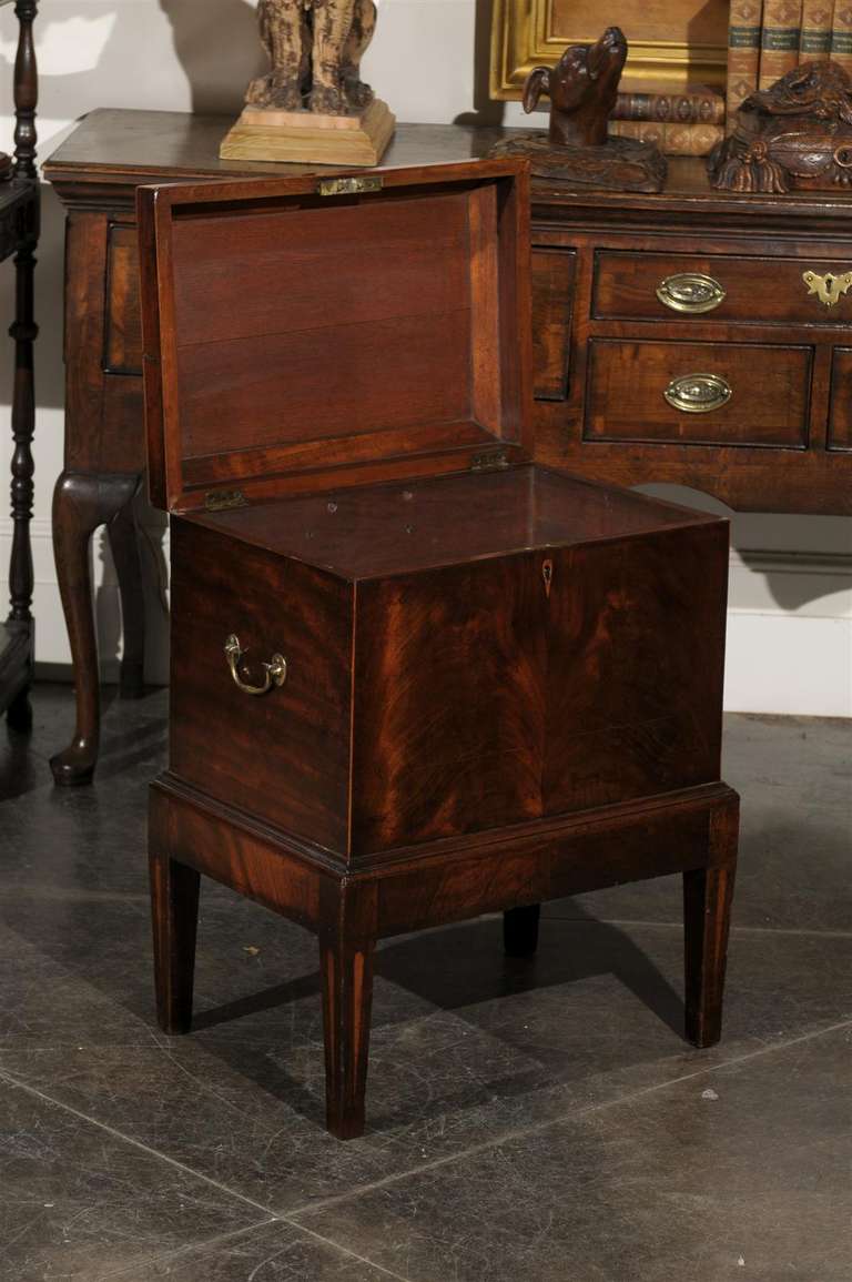 This early 19th century Georgian cellarette is composed of a figured mahogany rectangular box with a cavetto moulded hinged top resting on a short Stand with square tapered feet. The front presents a plain keyhole while the sides both feature brass