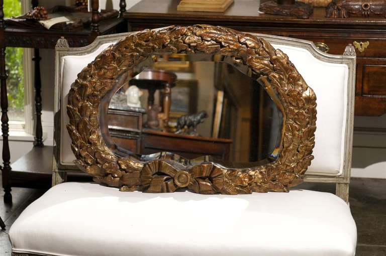 An Italian gilt mirror with an oval oak leaf frame from the 19th century. This mid-19th century carved giltwood Italian mirror is set within an unusual oval oak leaf wreath frame, tied with a ribbon in the lower part. The richly decorated frame
