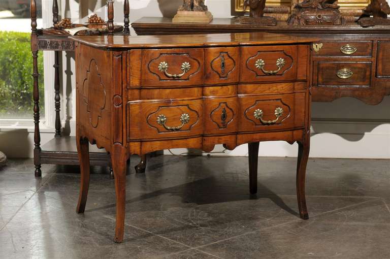 This exquisite French early 19th century commode features a serpentine front made of two drawers. Each drawer is decorated with geometrical motifs surrounding the hardware of bail handles and flower shaped plates, as well as the central escutcheon.