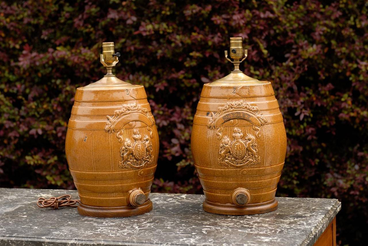 A pair of English stoneware spirit barrel lamps from the mid-19th century. The glazed bodies are shaped like barrels decorated with low-reliefs depicting the United Kingdom’s royal coat of arms, complete with a lion on the left and a unicorn on the