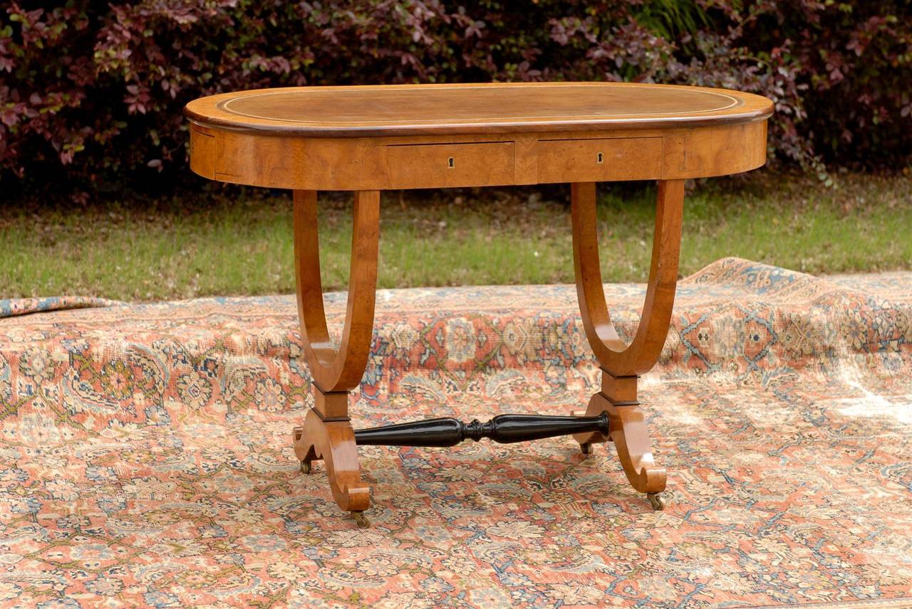 This Austrian Biedermeier desk or writing table features an exquisite birch top with brown leather in the centre, over an apron fitted with six dovetailed drawers in its surround. The table is raised on two semi-circular legs resting on scrolled