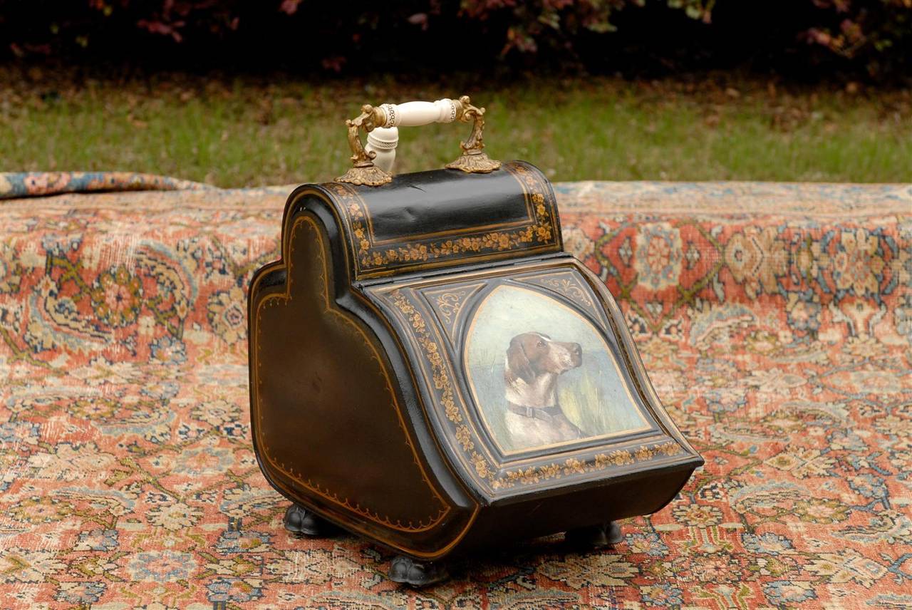 This exquisite English coal scuttle (or coal hod) from the late 19th century is painted tole with an elaborte carrying handle. The body is delicately adorned with a frieze of floral motifs while the centre of the lift-top panel is decorated with a