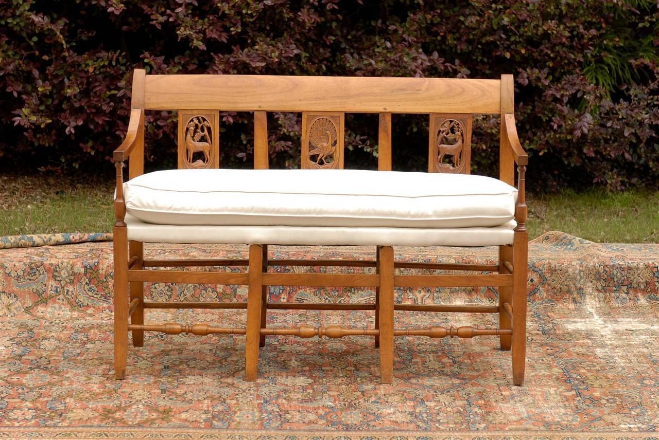 This French wooden bench from the mid-19th century features an exquisite slightly out-scrolled back with delicate carving marking the three seats. Two carved deer flank a central peacock, who generously makes a wheel, a perfect demonstration of the