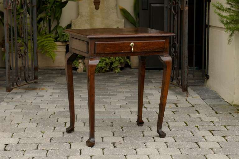 A mid-19th century oak side table presenting a two-plank rectangular molded and crossbanded top. The frieze drawer is adorned with a delicate brass drop bail topping a molded front echoed on the sides with similar rectangular moldings. Raised by