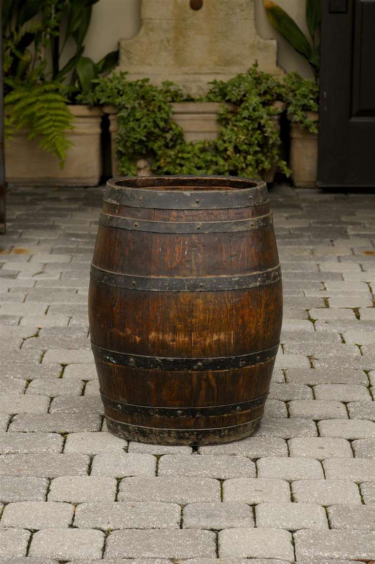 An English wooden rustic barrel with metal straps. This late 19th century barrel is made of vertical wooden slats - possibly oak - secured by six horizontal iron bands.  Given the strength of its construction this barrel may have been used to