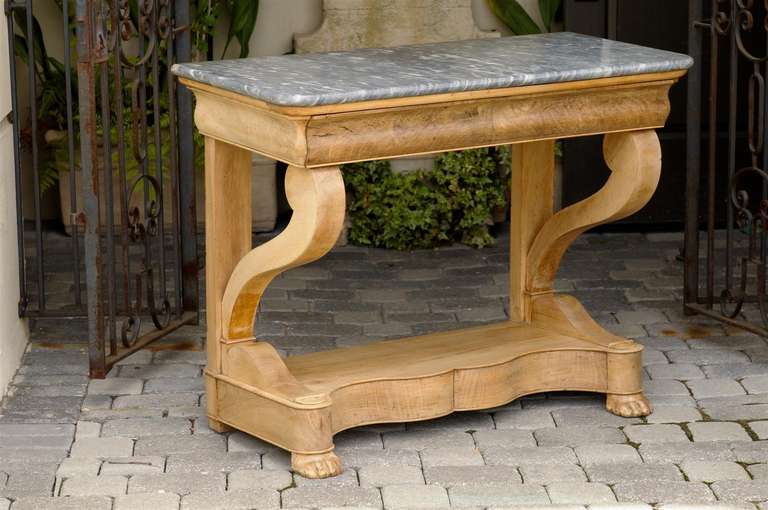 A French Charles X walnut console table with light grey marble top and paw feet from the first half of the 19th century. This French carved walnut console table features a rectangular light grey marble top with rounded corners over a blond walnut