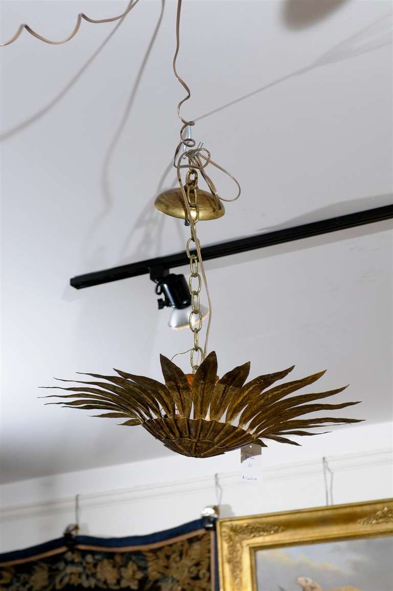 This Spanish semi-flush gilt metal Sunburst light fixture from the mid-20th century consists of a ribbed campaniform bowl surrounded by a crown of hammered curving pointing leaves. The recently rewired fixture is suspended by a chain attached to a