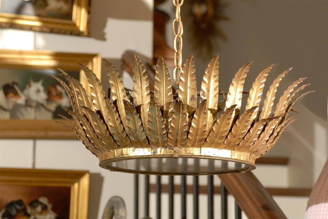 This Spanish three-light gilt metal semi-flush crown chandelier from the mid-20th century is decorated by two layers of thin leaf motifs on the surround. A first ring of shorter leaves gives birth to a second layer of taller ones. The frosted glass