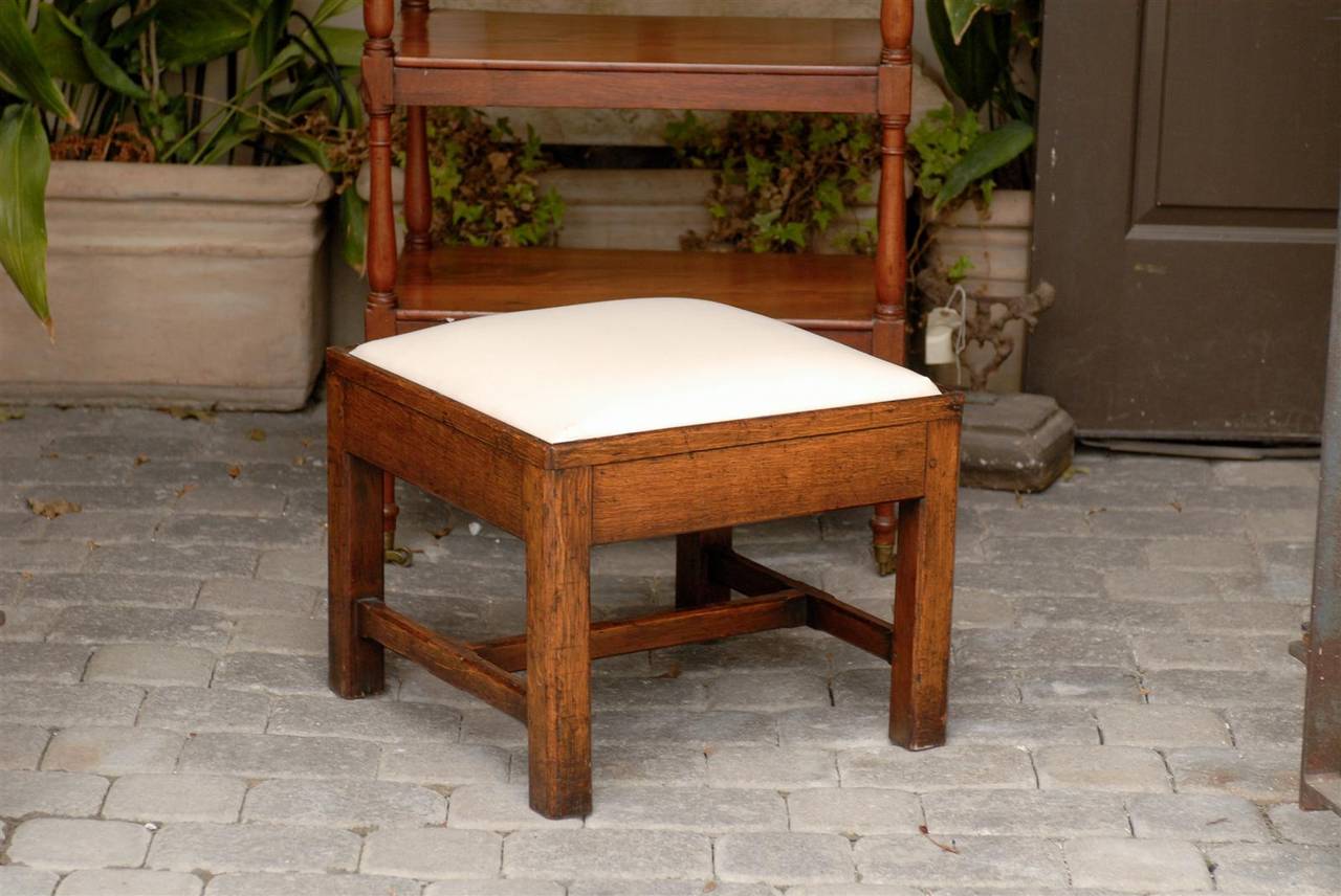 An English oak stool or ottoman with upholstered seat from the late 19th century. This English stool from the 1880s with square upholstered seat is made of oak and stands on four straight legs. The legs are strengthened by a cross stretcher. The