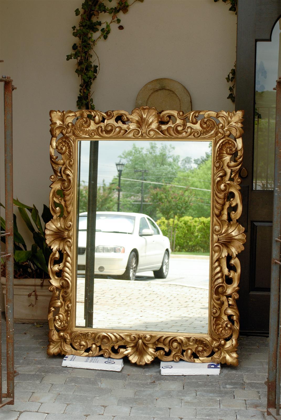 This large size Italian mirror from the second half of the 19th century, features a richly carved rectangular giltwood frame, adorned with a variety of foliage and shell motifs, typical of the Rococo style. Four shells mark the centre of each side,