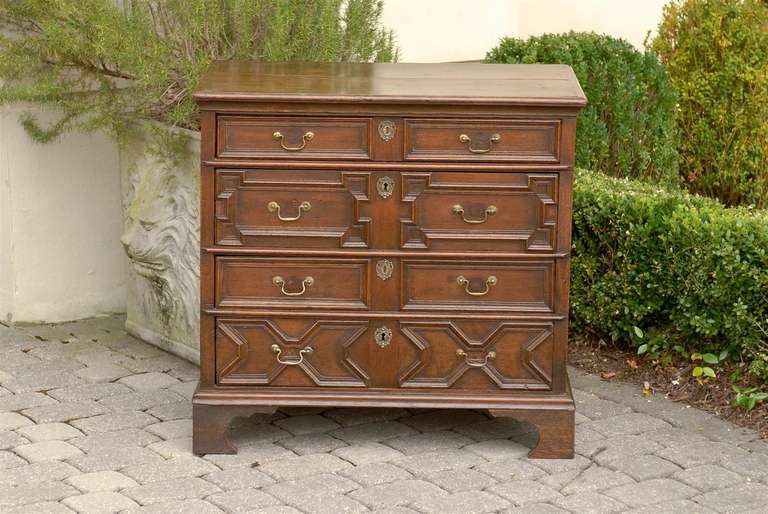This English early 19th century geometric front oak chest features a rectangular top with rounded edges over four dovetailed drawers, grooved on the side for the runner. The geometric drawers discreetly alternate to provide a nice rhythm: a smaller