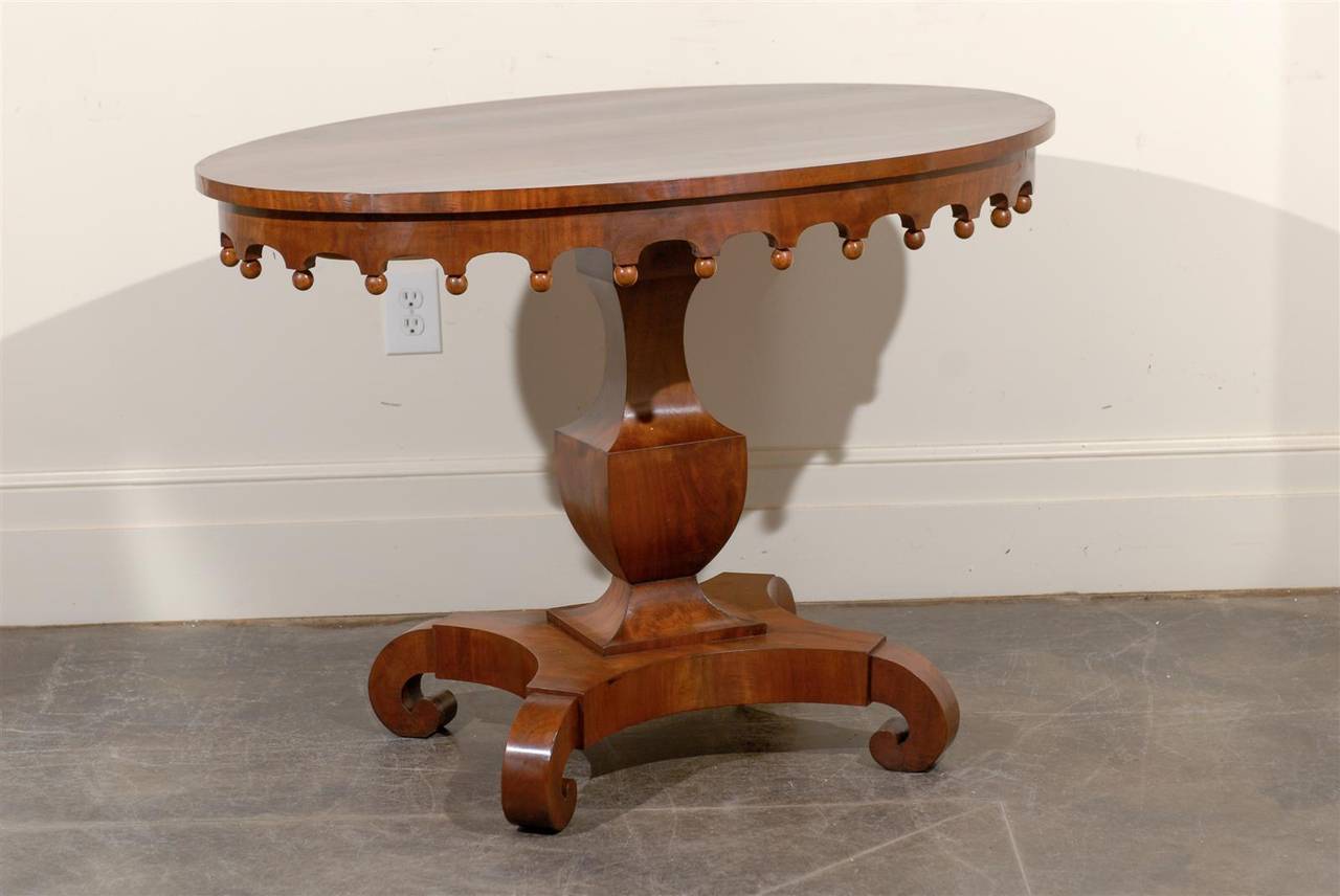 Oval pedestal table with scalloped apron and curved foot base.