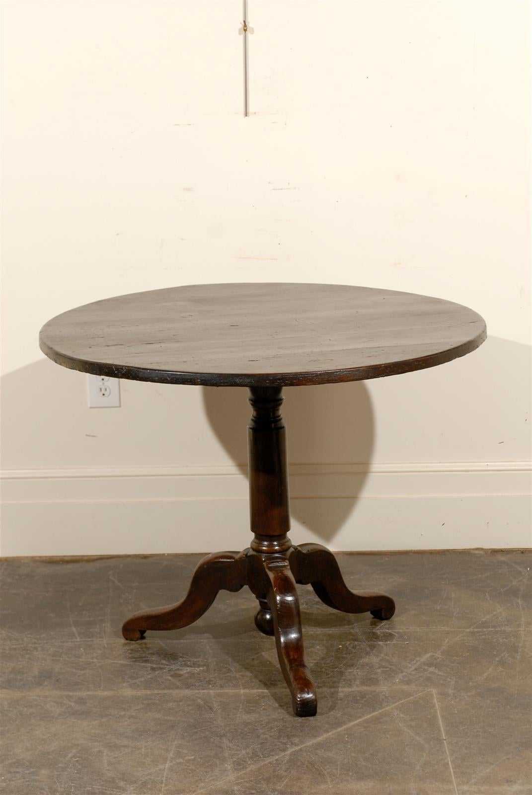 A wooden French round pedestal table from the turn of the century (19th to 20th). This side table features a simple round top supported by a pedestal base wit tripod scrolled feet. The lines on this French table circa 1890 - 1910 are simple yet