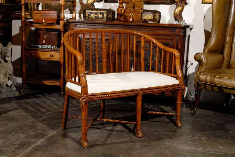 A stylish, early 20th century French wooden settee with a faux bamboo frame featuring an openwork tub-shaped backrest with sloping arms and a recent white muslin upholstery. It's raised on six bamboo-turned tapered legs, with three in the rear being
