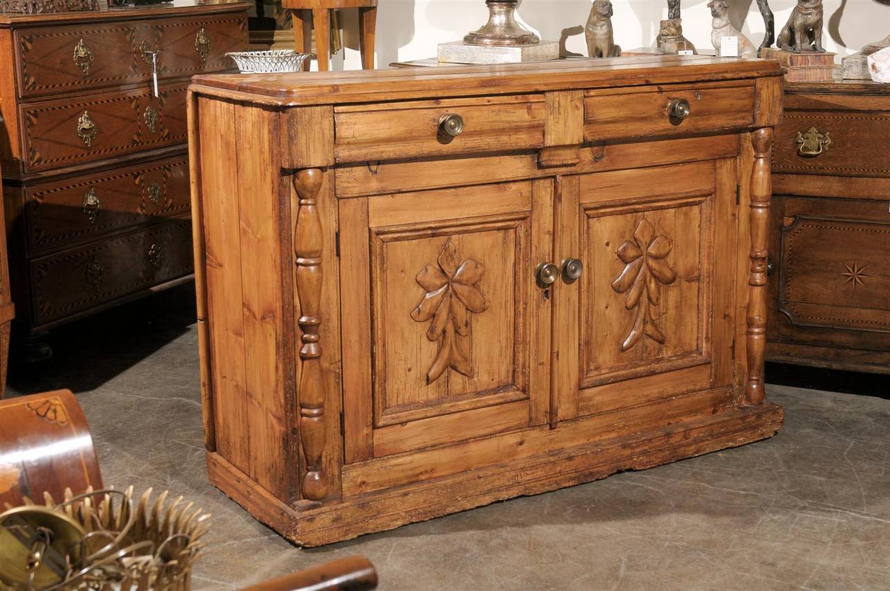 This nicely carved pine buffet from the mid-19th century features a raised rectangular top with rounded edges over two drawers with brass pulls, atop two doors. The simplicity of the pine structure is perfectly balanced by the elegant choice of the