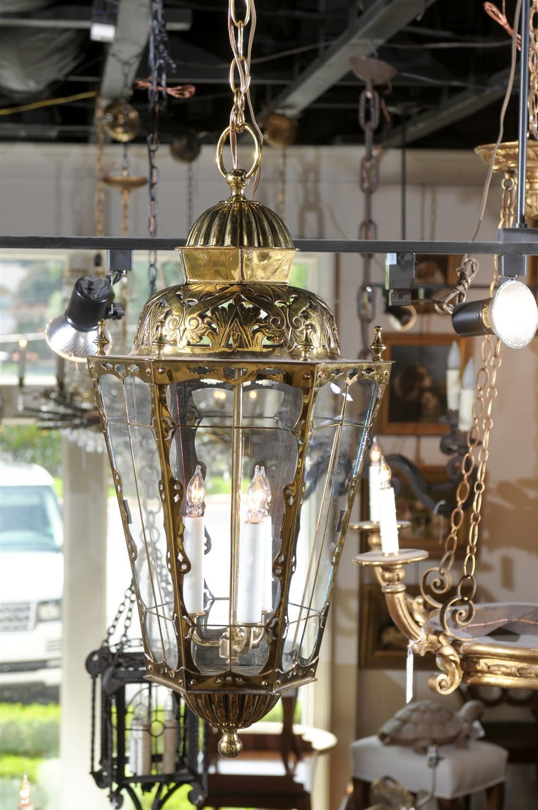 This exquisite English brass three-light lantern from the late 19th century features an hexagonal body with glass panels and pierced top. The intricate design of the crest is made of stylized foliate motifs and various volutes. Each panel of the