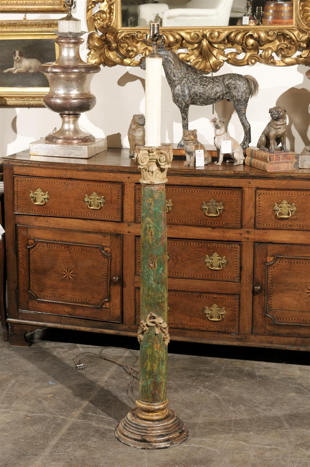 This exquisite Italian floor lamp from the early 19th century features a green painted wooden column supporting a carved Corinthian capital of tan color with acanthus leaves and volutes typical of this classical order. While the eye is immediately
