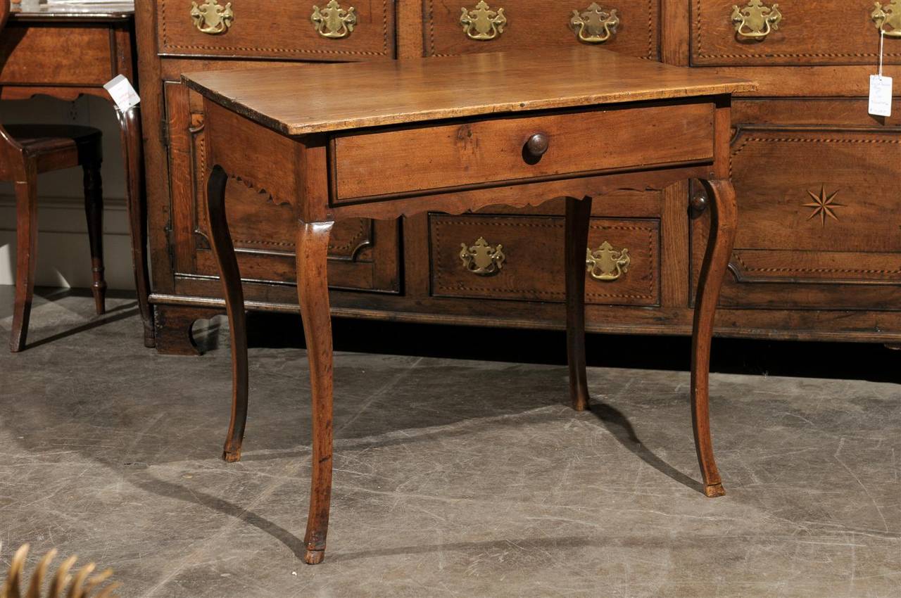 A French Restauration period walnut side table with single drawer and cabriole legs from the early 19th century. This elegant French side table circa 1820 features a sober rectangular top, over a nicely scalloped apron with single drawer. The table