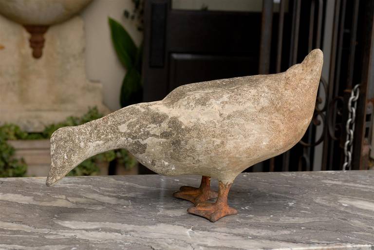 A lifesize carved stone duck sculpture with iron feet from the first half of the 20th century. This carved stone animal sculpture depicts a duck bending his head forward to peck at the ground in search of food. Perhaps we are along the banks of a