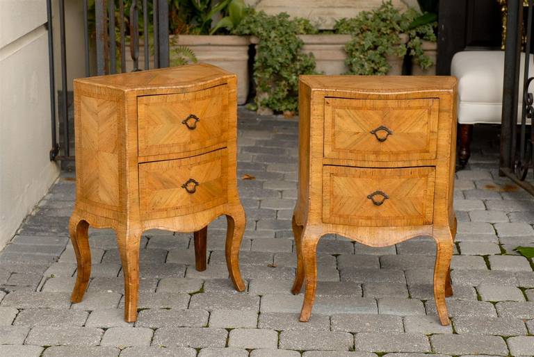 A pair of Italian 19th century Louis XV style two-drawer bombé commodes made of pale wood with the sides opening out towards the back in an undulating movement. Each chest is raised on four cabriole legs and an arbalest shaped frieze. The drawers