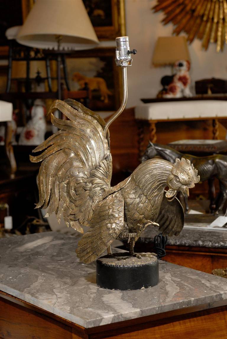 An Italian vintage brass rooster table lamp on old iron base. This beautiful Italian lamp is made of a brass rooster with an incredible plumage. The rooster has one foot raised, his head thrust forward and his wings are raised as he appears ready to