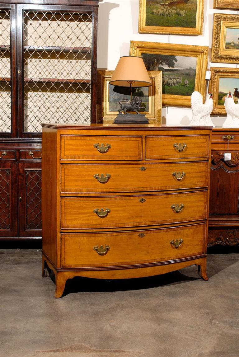 This mid-19th century English mahogany chest of five drawers features a bow-fronted rectangular crossbanded top with ebony inlays and a molded edge above a conforming case of two smaller frieze drawers over three graduated drawers. Similarly