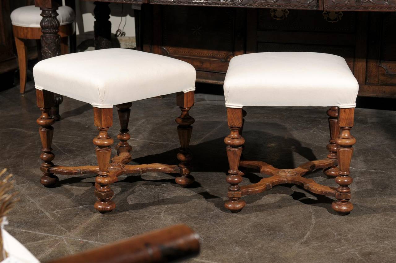 This pair of English walnut stools from the mid 19th century features upholstered square-shaped seats over four elegant turned legs. One can immediately sense the care and skill that was demonstrated during the construction of these stools,
