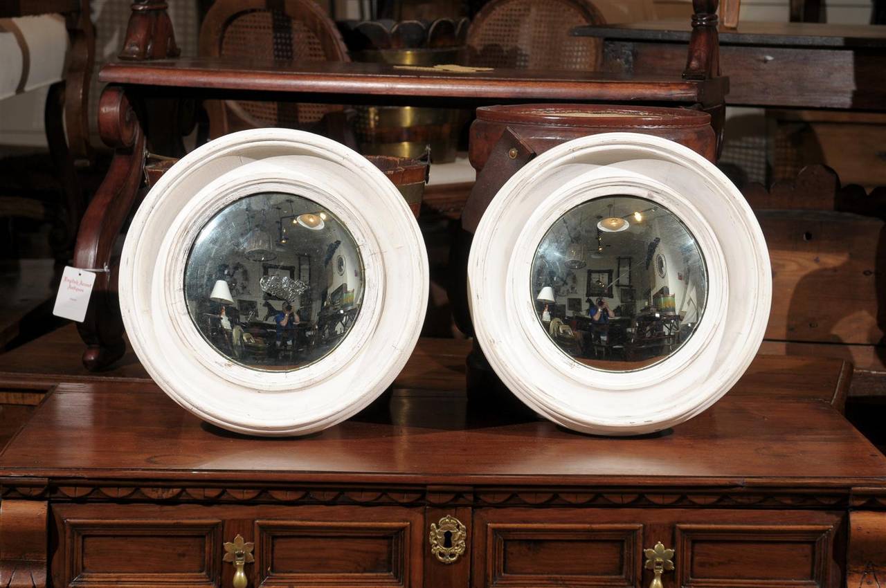 This pair of French mirrors from the late 19th century features two convex glass mirrors set in deep concave frames. Painted in a clean faded white these stylish mirrors, circa 1880 have an almost nautical sense about them. With their subtle white