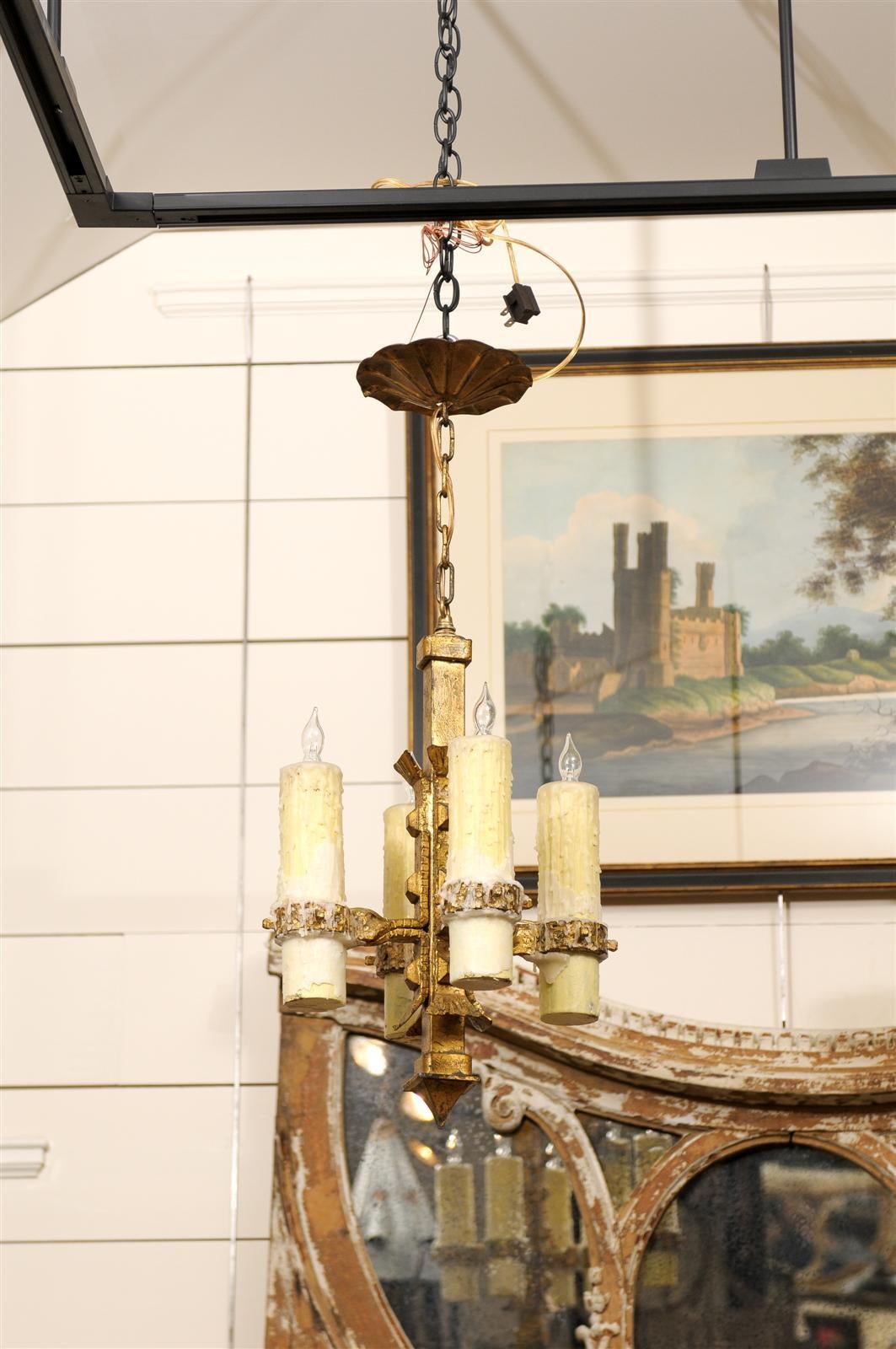 A vintage French gilt iron four-light small size chandelier. This French light chandelier from circa 1950 features a central gilded iron armature to which four arms are elegantly attached, each holding a large size authentic wax candle. This central