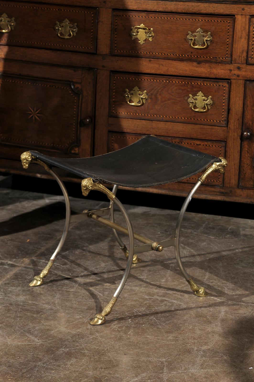 This Italian Directoire style steel stool from the mid-20th century feature a black leather seat attached to four brass ram’s heads sitting atop four nicely curved legs. The stool is raised on delicate brass hoof feet connected to one another