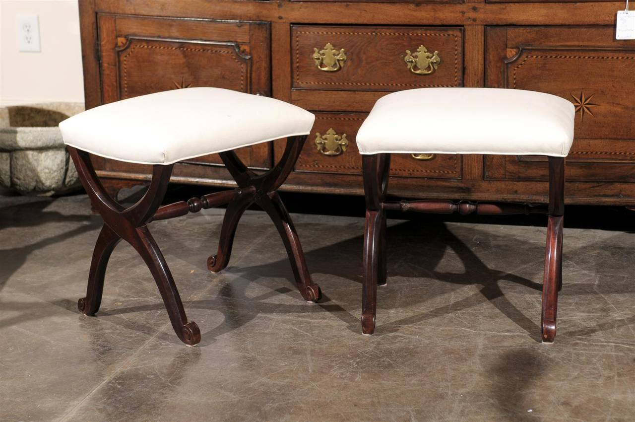 A pair of French carved mahogany X-Form stools from the late 19th century with new muslin upholstery. Each of this pair of stools features a rectangular seat, recovered with a single welt muslin upholstery. Each stool is raised on an X-Frame base