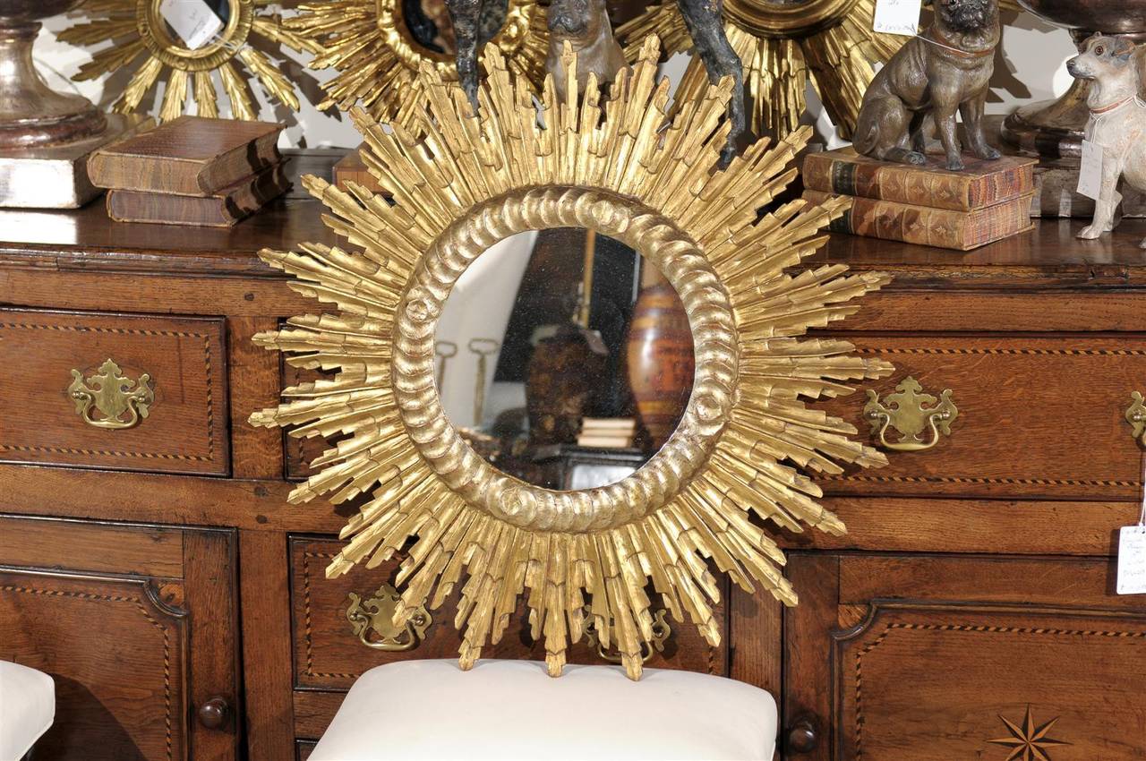 This French medium size giltwood sunburst mirror from the mid-20th century features a round new glass mirror in the centre, surrounded by a circular carved molding. From there, a myriad of carefully organized sunrays of various sizes extend
