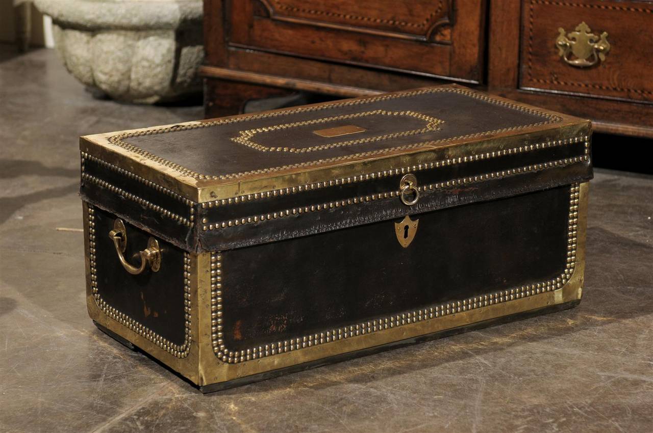 An English leather over camphor wood trunk with brass studs from the mid-19th century. This English rectangular brass bound trunk features two lateral carrying handles. The escutcheon has the shape of a shield. The top is adorned with additional