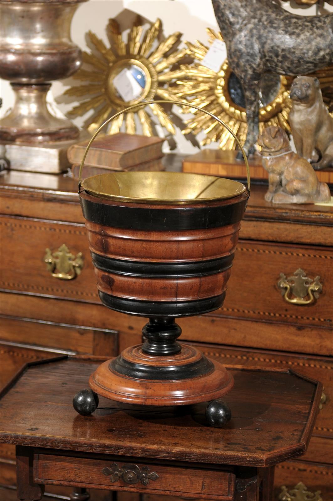 A 19th century English wooden peat bucket with brass lining. This walnut and ebonized wood peat bucket, circa 1860-1870 rests on three ball feet and has a removable brass lining. Peat buckets were common in England and Ireland during the 19th