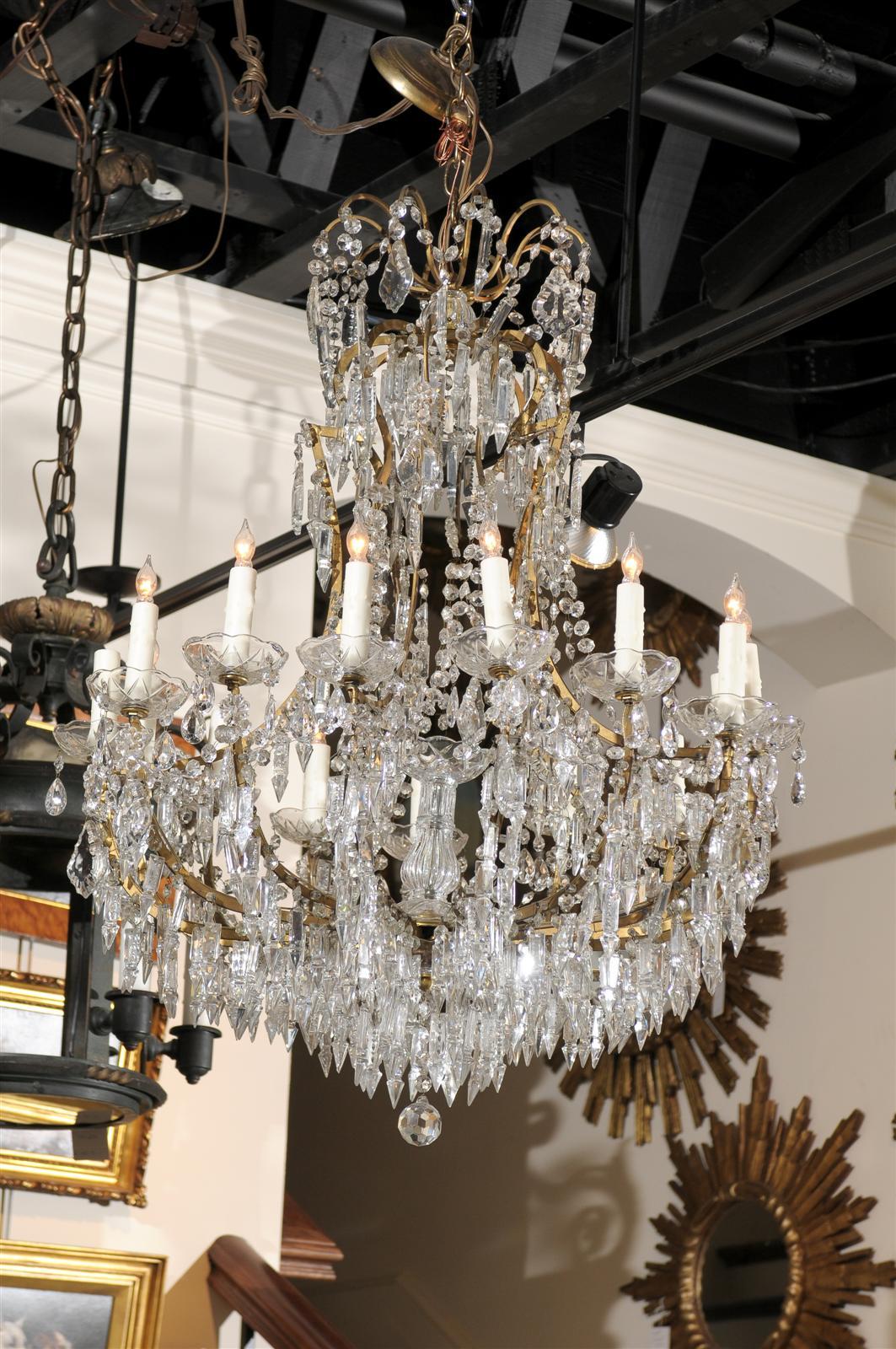 This French Louis XV style fifteen-light crystal chandelier from the early 20th century features a thin gilded metal armature, supporting a variety of crystals. The upper part of the chandelier is decorated with scrolled arms, supporting pendeloques