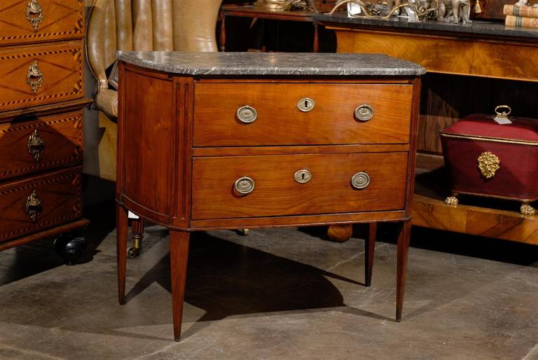 A French Empire style mid-19th century petite two-drawer commode with grey marble top. This elegant 19th century French two-drawer petite commode with a trapezoidal grey veined marble top is raised on four slender tapered legs. It features canted