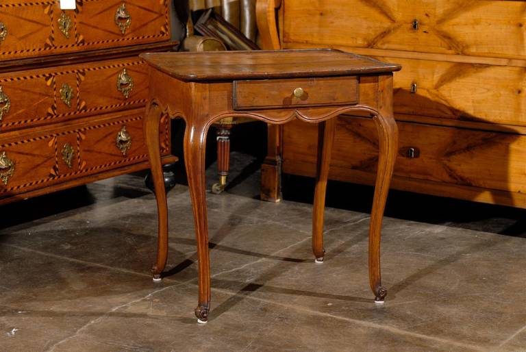 Elegant French walnut side table with single drawer from the mid 19th century. This French table features a rectangular top sitting on a scalloped apron adorned with a single drawer and brass pull. It rests on four cabriole legs with raised on