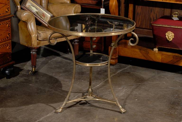 A French Directoire style guéridon brass table with stone top and lower tier from the mid-20th century. This French, 1950s, side table features a circular black stone top set inside a brass surround. The table is raised on three saber-shaped legs,